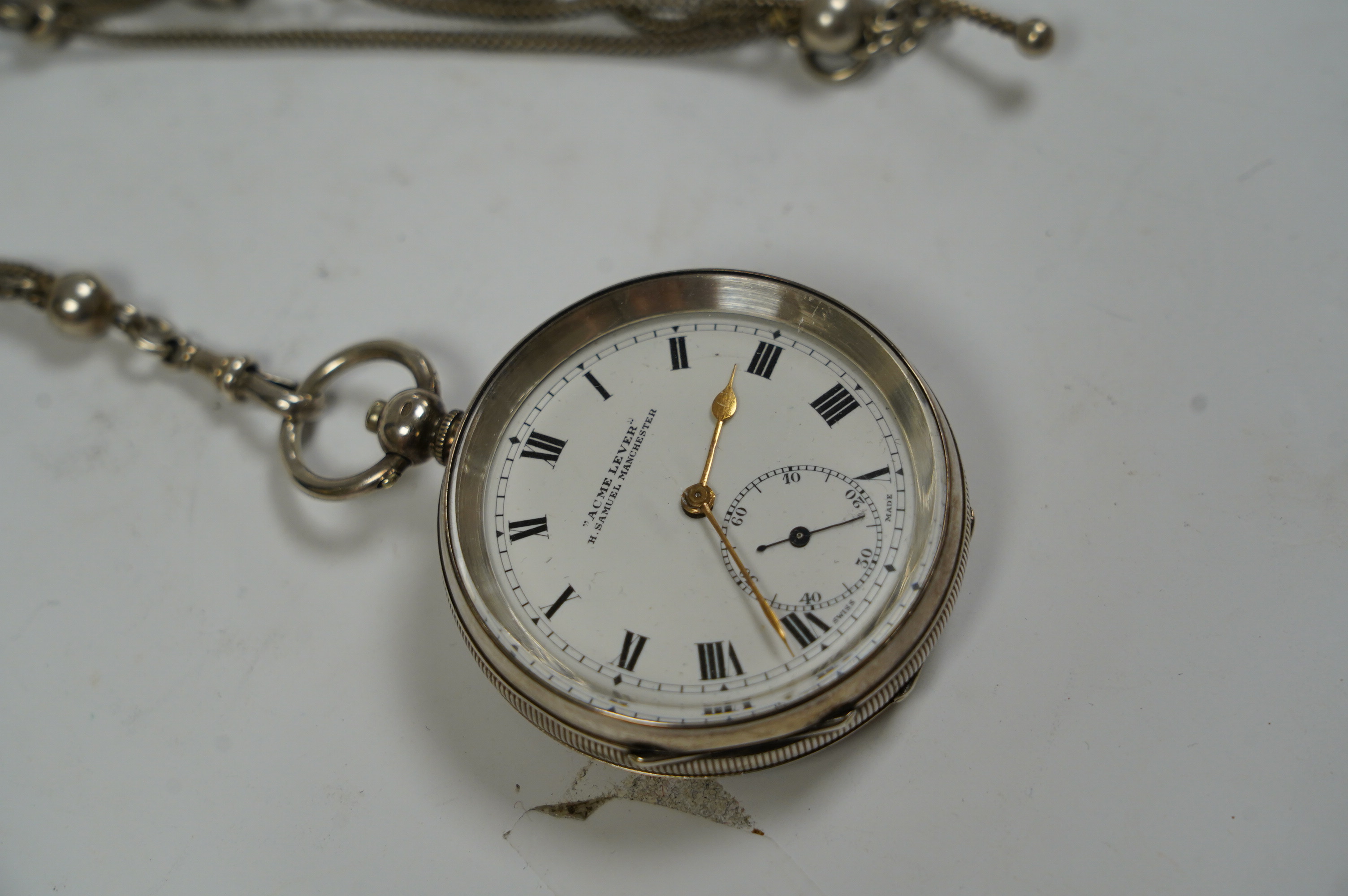 An early 20th century silver 'Acme Lever' open faced keywind pocket watch, retailed by Samuel, Manchester, with Roman dial and subsidiary seconds, case diameter 50mm, together with a white metal albertina. Condition - po